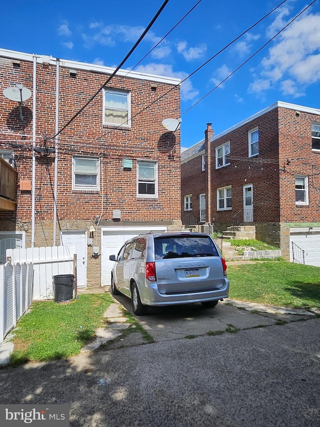 multi unit property featuring a garage, brick siding, driveway, and fence