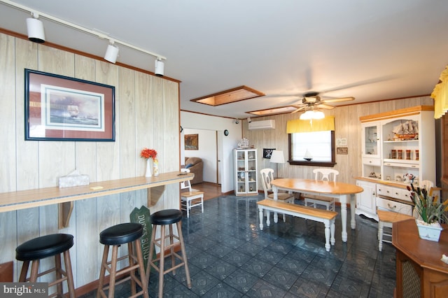 dining area with a ceiling fan, a wall unit AC, wooden walls, rail lighting, and a dry bar