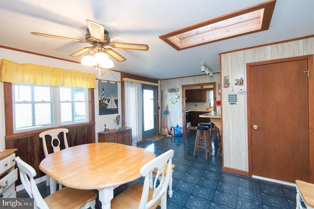 dining room with a skylight, a ceiling fan, dark floors, and wood walls