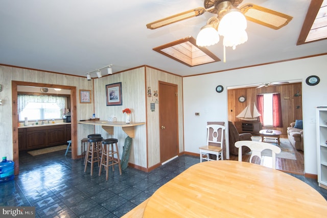 dining room featuring track lighting, crown molding, ceiling fan, baseboards, and a skylight