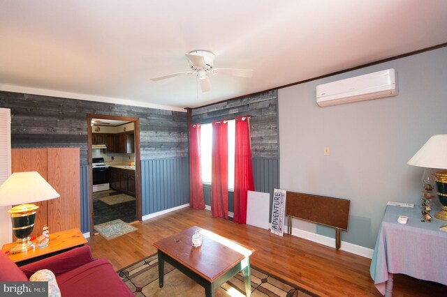 living area with a wall mounted air conditioner, baseboards, wood finished floors, and ceiling fan