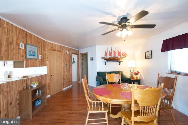 dining space with wooden walls, crown molding, baseboards, ceiling fan, and wood finished floors