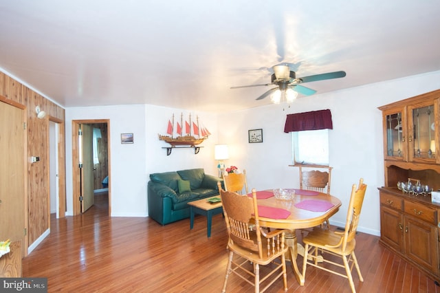 dining space featuring wooden walls, baseboards, light wood-type flooring, and a ceiling fan