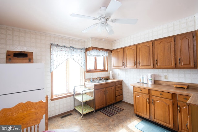 kitchen with brown cabinetry, visible vents, freestanding refrigerator, and wallpapered walls