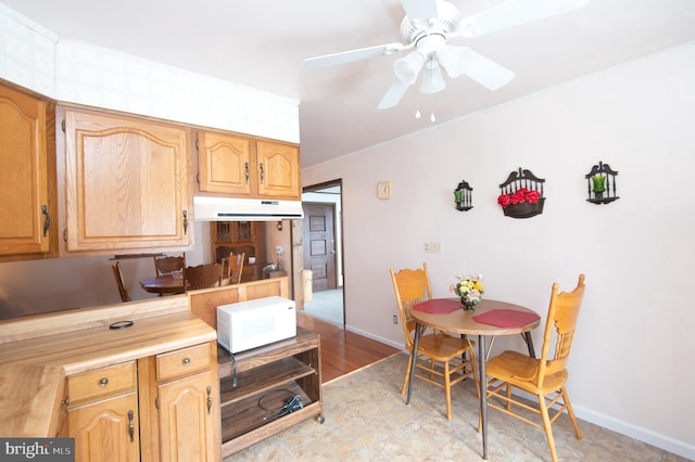 kitchen featuring under cabinet range hood, light countertops, baseboards, white microwave, and ceiling fan