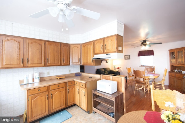 kitchen featuring under cabinet range hood, light wood-style floors, brown cabinetry, light countertops, and ceiling fan