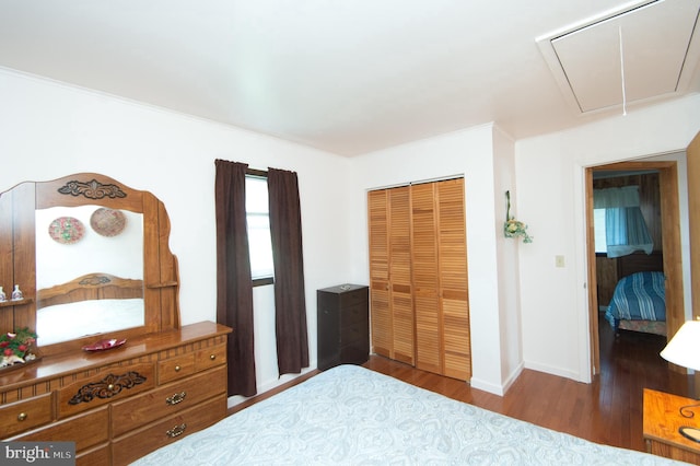 bedroom with a closet, attic access, baseboards, and wood finished floors