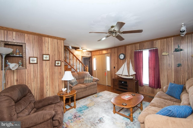 living area featuring wood finished floors, ceiling fan, stairs, wood walls, and crown molding