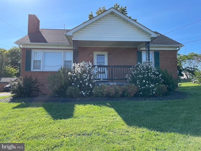 view of front of home with roof with shingles, a porch, a chimney, a front lawn, and brick siding