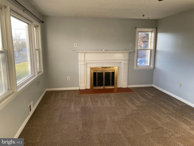 unfurnished living room featuring baseboards, a brick fireplace, and dark carpet