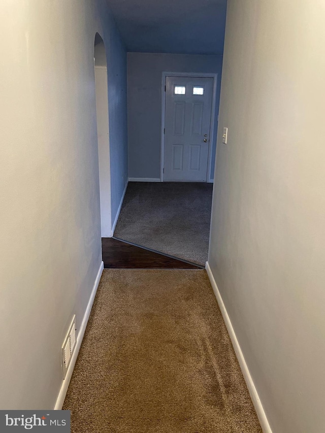 corridor with baseboards, carpet floors, arched walkways, and visible vents