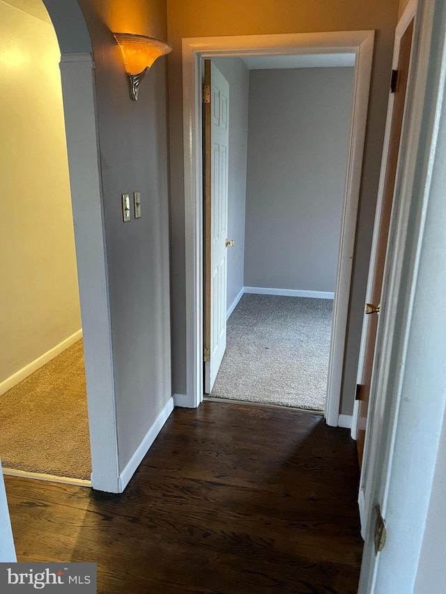 hall featuring arched walkways, baseboards, and dark colored carpet