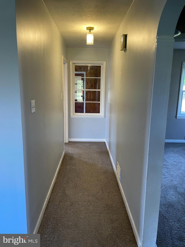 hallway with visible vents, baseboards, arched walkways, a textured ceiling, and dark colored carpet