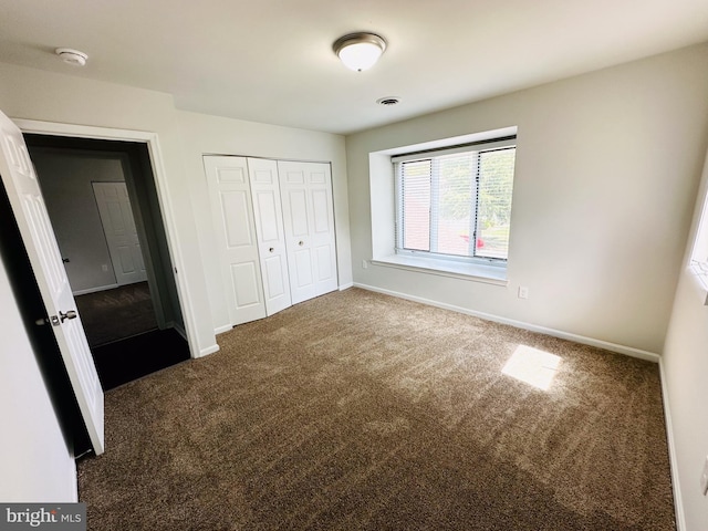 unfurnished bedroom featuring dark carpet and a closet