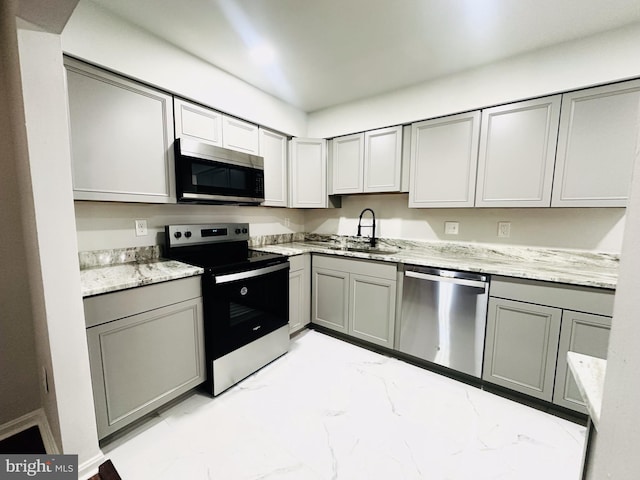 kitchen with appliances with stainless steel finishes, gray cabinetry, sink, and light stone countertops