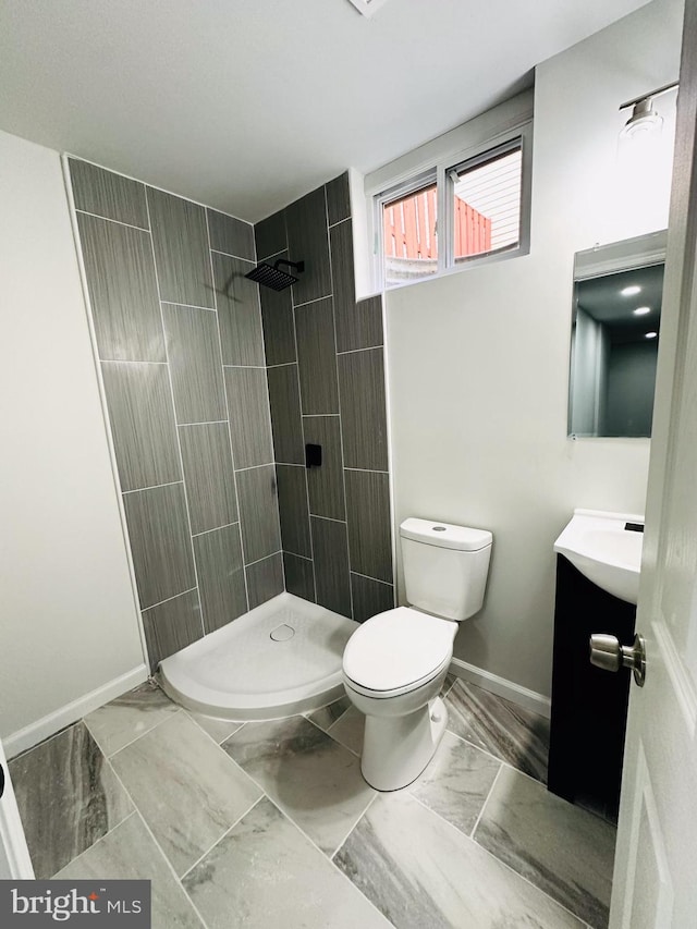 bathroom featuring a tile shower, vanity, and toilet