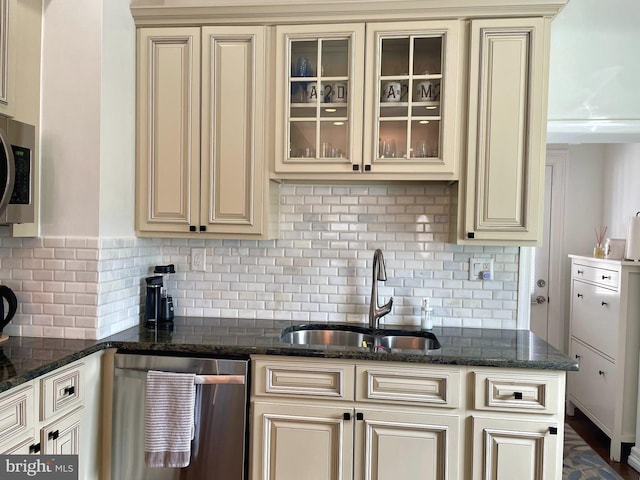 kitchen featuring dark stone countertops, backsplash, stainless steel appliances, sink, and cream cabinetry