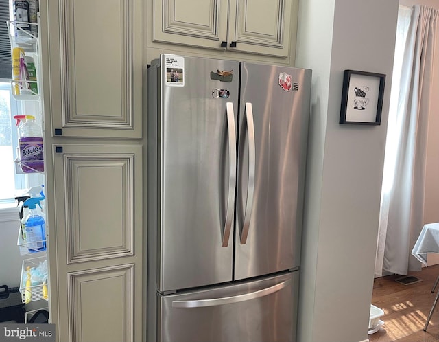 kitchen with cream cabinetry, hardwood / wood-style flooring, and stainless steel refrigerator