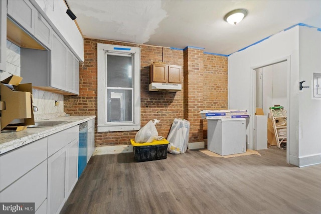 kitchen with white dishwasher, light hardwood / wood-style flooring, ornamental molding, light stone counters, and brick wall