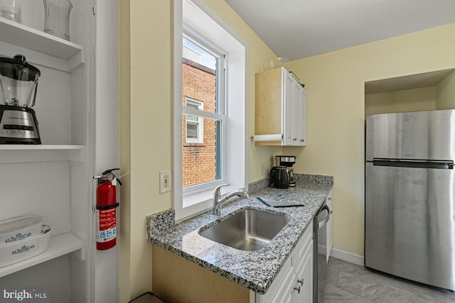 kitchen with stainless steel fridge, light stone countertops, sink, and white cabinets