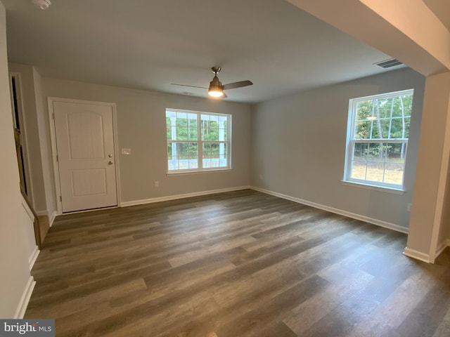 empty room with dark wood finished floors, visible vents, a ceiling fan, and baseboards