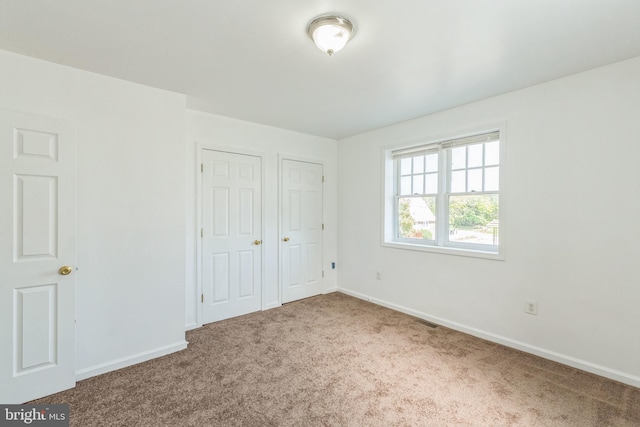 unfurnished bedroom with two closets and carpet flooring