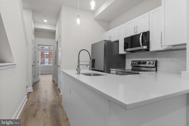 kitchen with white cabinets, appliances with stainless steel finishes, hanging light fixtures, and light hardwood / wood-style floors