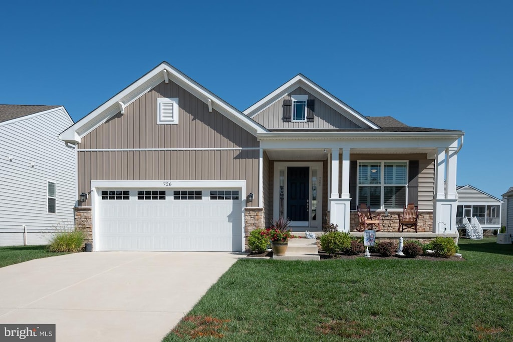 craftsman-style house featuring a front lawn, a porch, concrete driveway, stone siding, and an attached garage