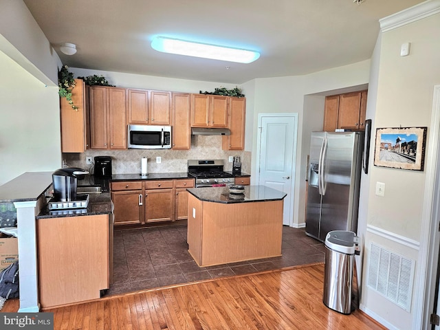 kitchen featuring appliances with stainless steel finishes, a kitchen island, backsplash, and dark hardwood / wood-style flooring