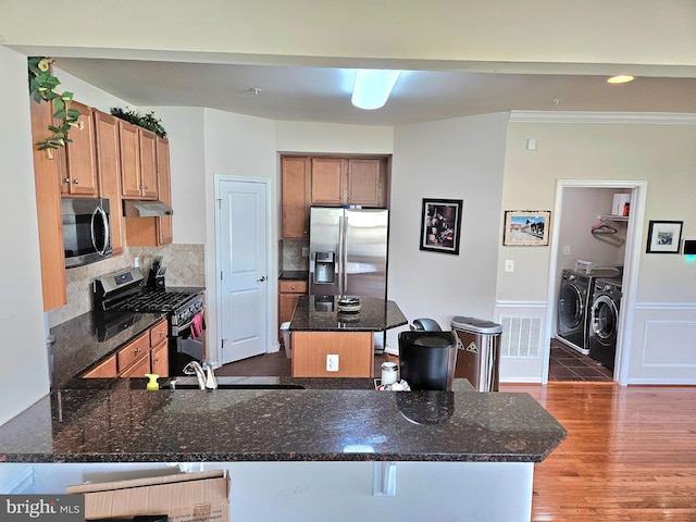 kitchen featuring dark stone counters, washer and dryer, kitchen peninsula, dark wood-type flooring, and appliances with stainless steel finishes