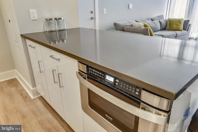 kitchen featuring light wood-type flooring, oven, and white cabinetry