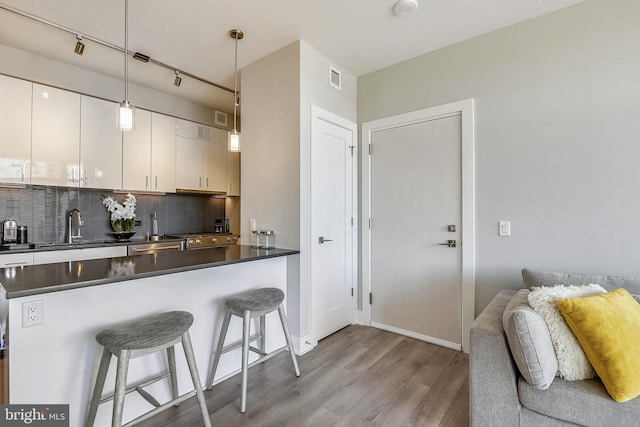 kitchen featuring rail lighting, sink, a breakfast bar, white cabinets, and light hardwood / wood-style floors