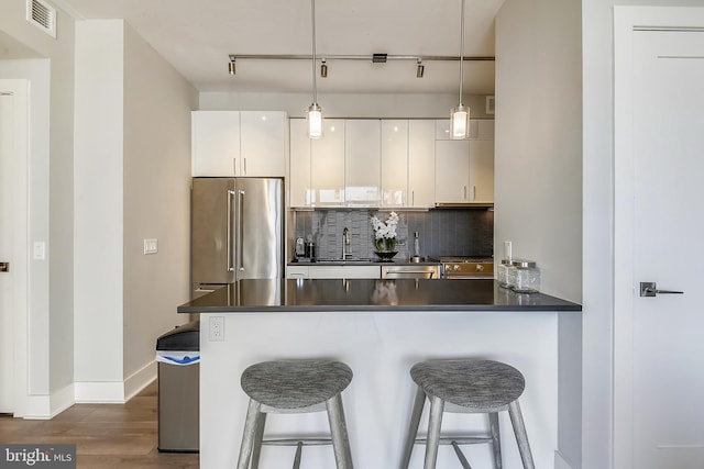 kitchen with white cabinetry, kitchen peninsula, decorative backsplash, appliances with stainless steel finishes, and a breakfast bar area