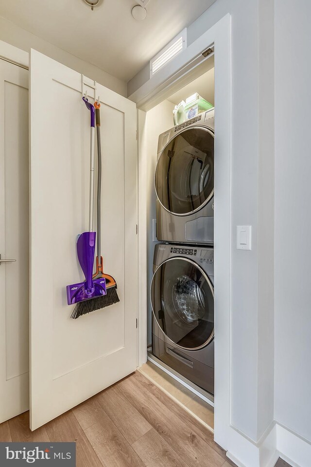 clothes washing area with stacked washing maching and dryer and light hardwood / wood-style flooring