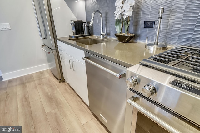 kitchen with light wood-type flooring, appliances with stainless steel finishes, white cabinetry, and sink