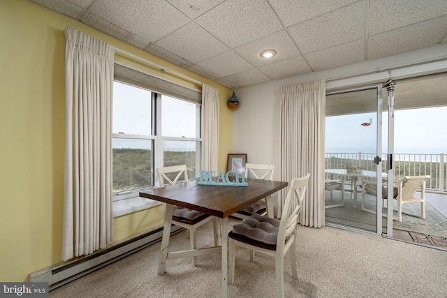 carpeted dining area featuring a drop ceiling, baseboard heating, and a wealth of natural light