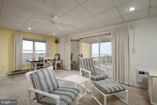 living area featuring a drop ceiling, a ceiling fan, a wall mounted air conditioner, and a baseboard radiator