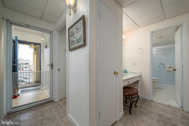 corridor with a drop ceiling, baseboards, visible vents, and tile patterned flooring