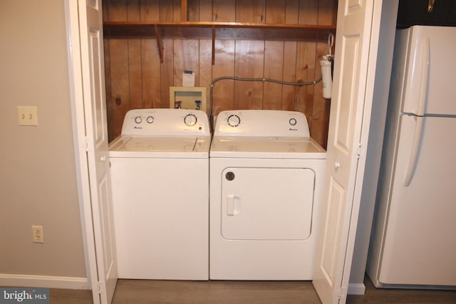 clothes washing area featuring washer and dryer, laundry area, wooden walls, and wood finished floors