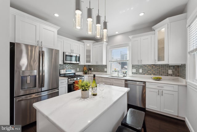 kitchen with hanging light fixtures, stainless steel appliances, a center island, dark hardwood / wood-style floors, and white cabinets