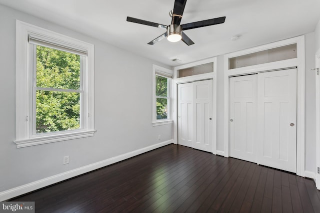 unfurnished bedroom with two closets, ceiling fan, and dark hardwood / wood-style flooring