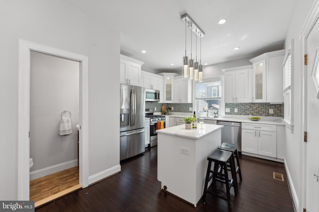 kitchen featuring a kitchen island, dark hardwood / wood-style floors, decorative light fixtures, appliances with stainless steel finishes, and white cabinetry