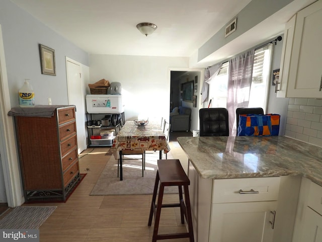 kitchen featuring stone countertops, visible vents, backsplash, and white cabinetry