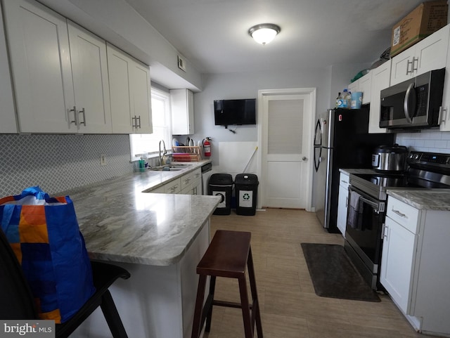 kitchen with a kitchen breakfast bar, appliances with stainless steel finishes, kitchen peninsula, sink, and white cabinetry