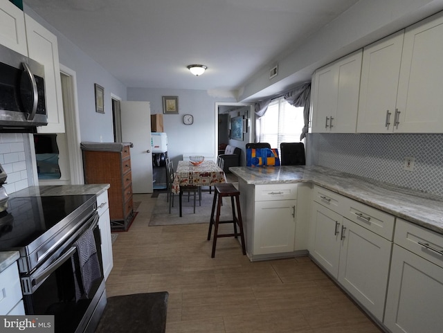 kitchen with a breakfast bar area, appliances with stainless steel finishes, tasteful backsplash, kitchen peninsula, and white cabinetry