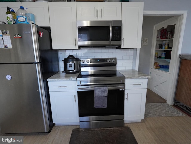 kitchen with light wood-type flooring, appliances with stainless steel finishes, tasteful backsplash, and white cabinetry