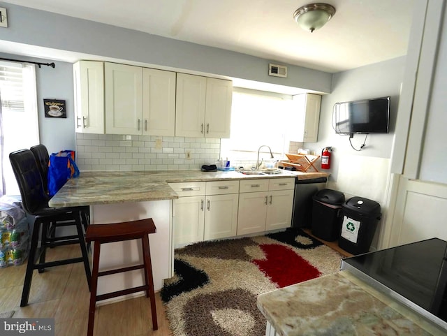 kitchen with visible vents, a sink, a kitchen breakfast bar, backsplash, and a peninsula