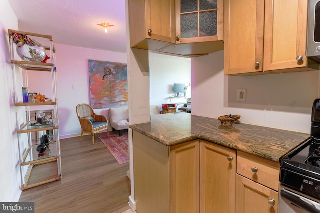 kitchen with kitchen peninsula, black gas range, dark stone counters, and light hardwood / wood-style floors