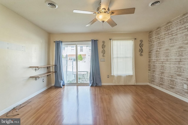 unfurnished room with wooden walls, visible vents, a ceiling fan, and wood finished floors