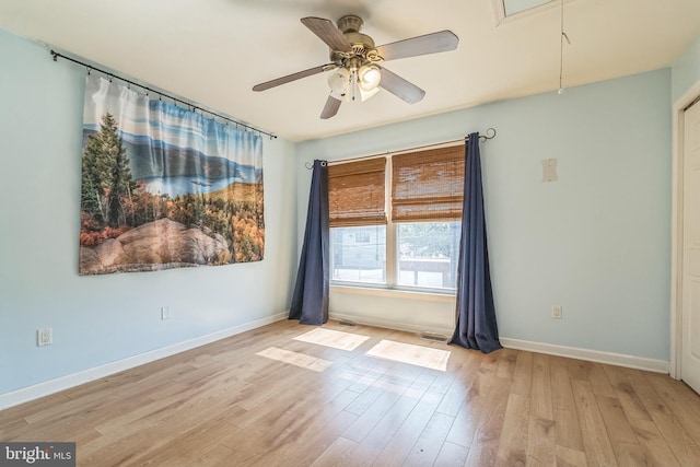 spare room with visible vents, baseboards, attic access, wood finished floors, and a ceiling fan